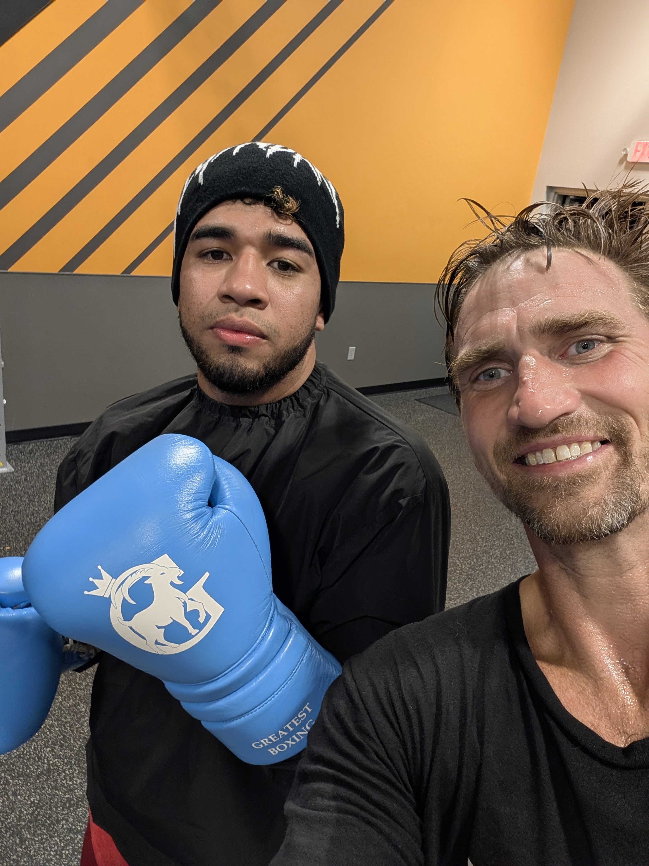 Jonathon Guyer with a boxing student holding up a blue boxing glove at the gym